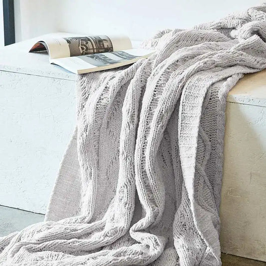 Cozy gray cable knit blanket draped over a white sofa with a magazine underneath.