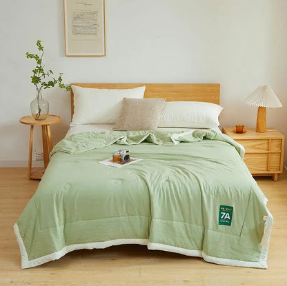 Bedroom with a bed covered in a green comforter, pillows, and a small table with a plant.