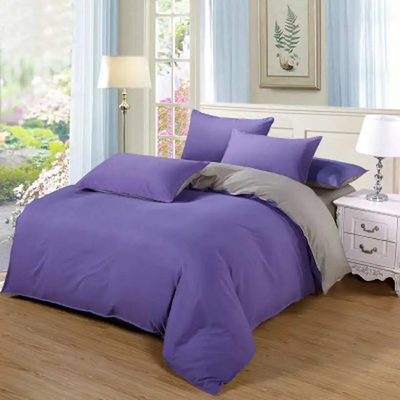 Purple bedding set on a bed in a bedroom with a window and lamp in the background.