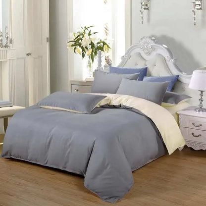 Gray bedding set on a bed in a bedroom with a lamp and plant in the background.