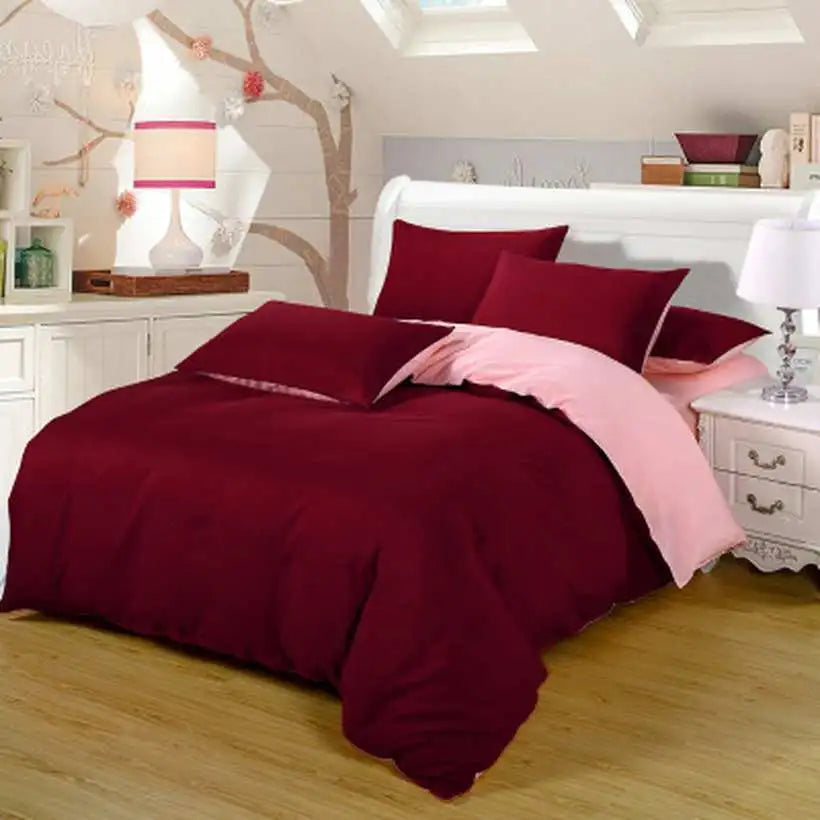 Maroon and pink bedding set on a bed in a bedroom with wooden floor and white walls.