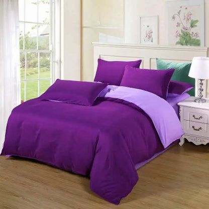 Purple bedding set on a bed in a well-lit bedroom with a lamp and window.