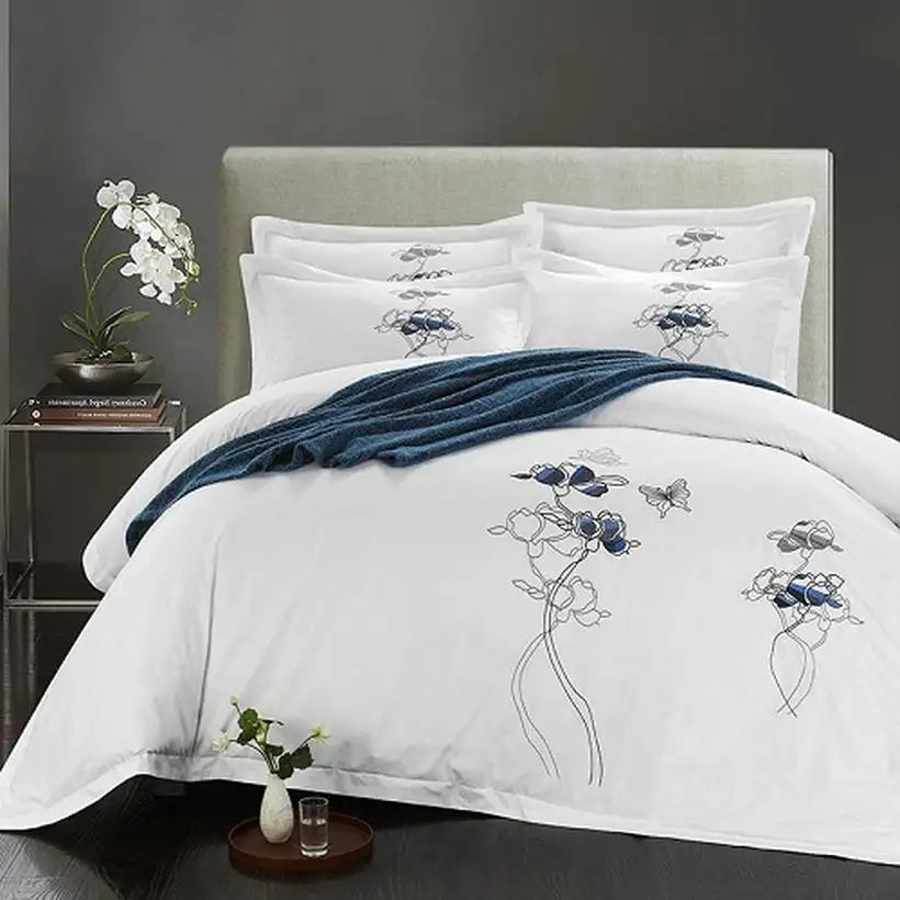 White bedding set with floral embroidery on a bed in a bedroom setting.