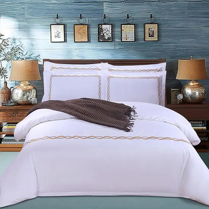 White bedding set with gold trim on a bed in a bedroom setting.
