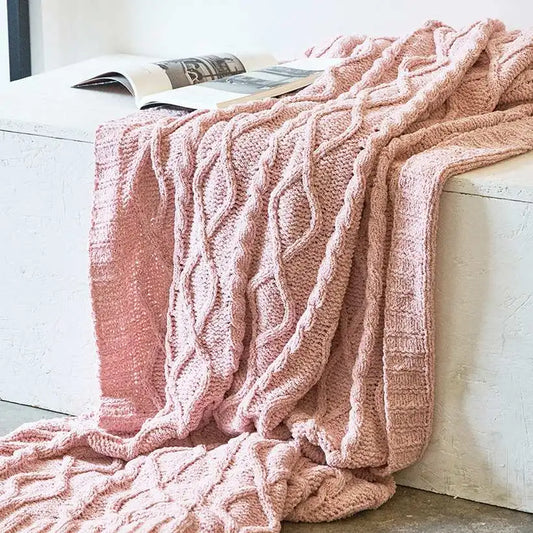 Pink knitted blanket draped over a white surface with a magazine underneath.