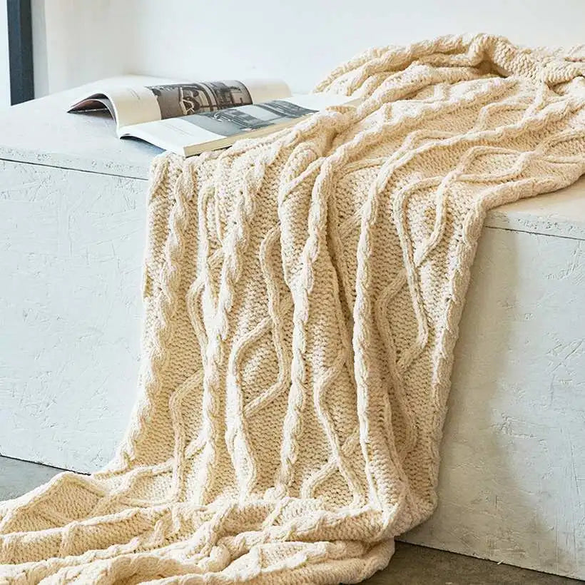 Beige cable knit blanket draped over a white surface with books underneath.
