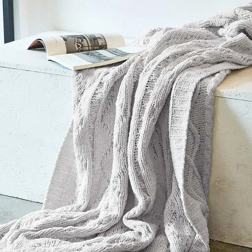 Cozy gray cable knit blanket draped over a white sofa with a magazine underneath.