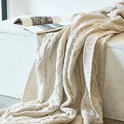 Beige knitted blanket draped over a white sofa with a magazine on a small table.