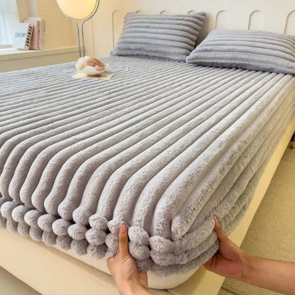 Folded gray textured blanket held by a person on a bed.