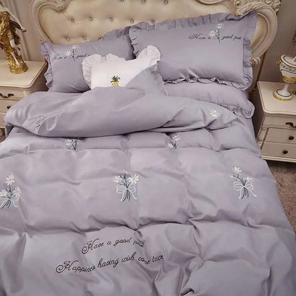 Gray bedding set with floral embroidery and text on a bed in a bedroom setting.