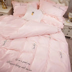 Pink bedding set with embroidered designs and text in a bedroom setting.