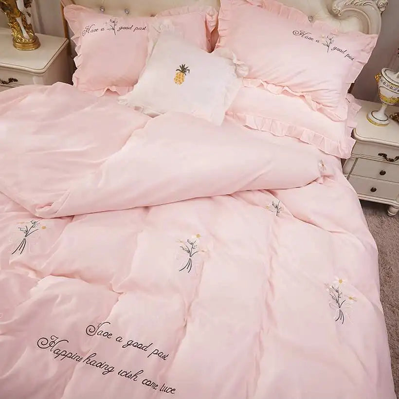 Pink bedding set with embroidered designs and text in a bedroom setting.