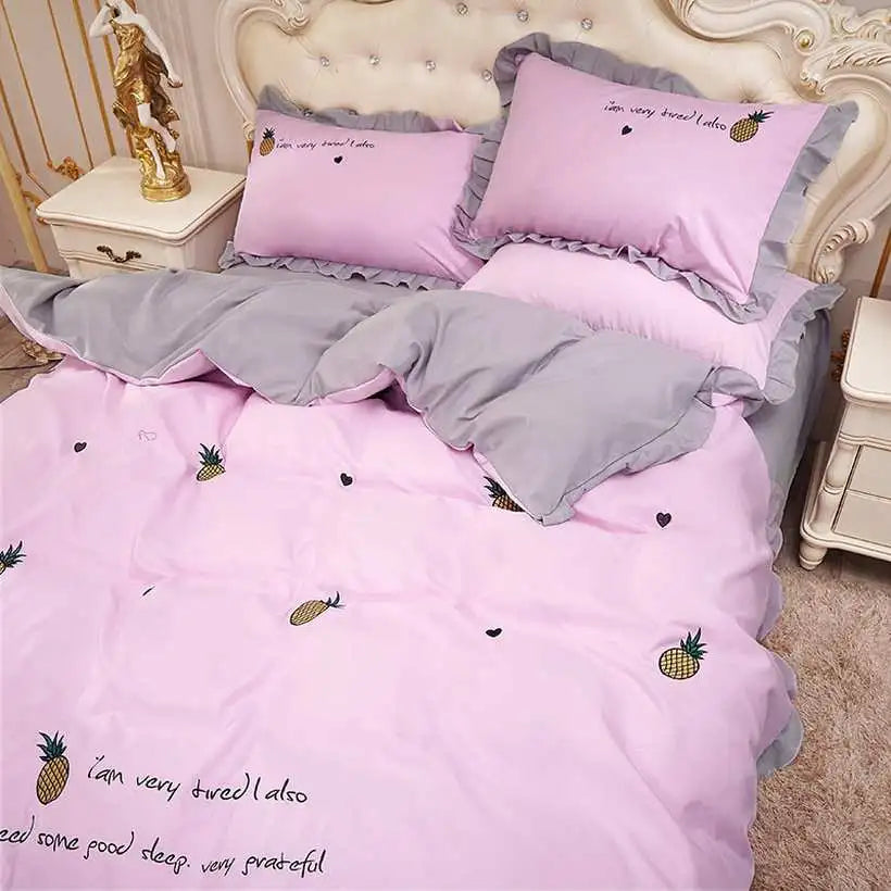 Pink and gray bedding set with pineapple designs on a bed.