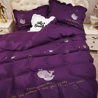 Purple bedding set with whale designs and text on a bed in a bedroom setting.