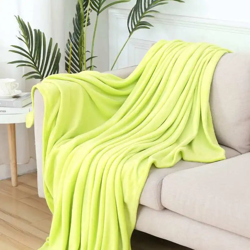 Light green blanket draped over a sofa in a living room setting with plants and a coffee table.