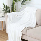 White blanket draped over a beige sofa with plants in the background
