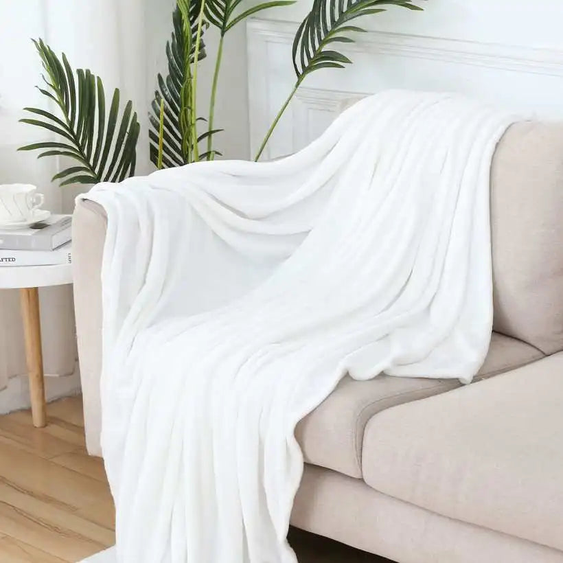 White blanket draped over a beige sofa with plants in the background