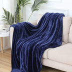 Navy blue blanket draped over a beige sofa in a living room setting with plants and a coffee table.