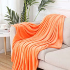 Orange blanket draped over a white sofa with a plant in the background