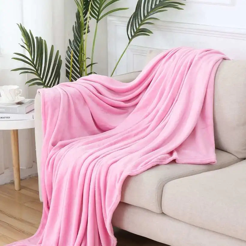 Pink blanket draped over a beige sofa in a living room setting with plants and a small table.