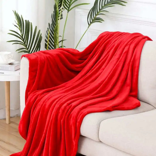 Red blanket draped over a white sofa in a living room with plants in the background.
