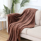 Brown blanket draped over a white sofa in a living room with plants and a coffee table.