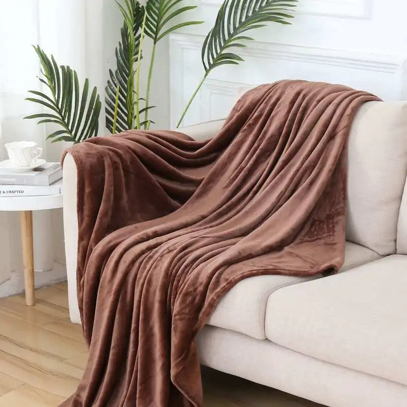 Brown blanket draped over a white sofa in a living room with plants and a coffee table.