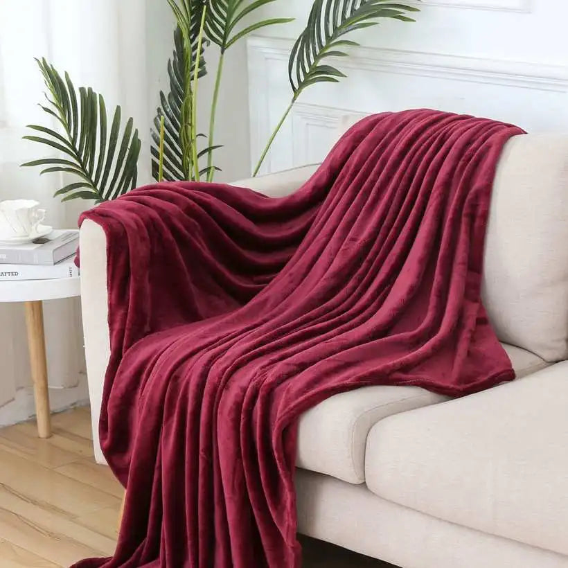 Red blanket draped over a white sofa in a living room with plants and a side table.