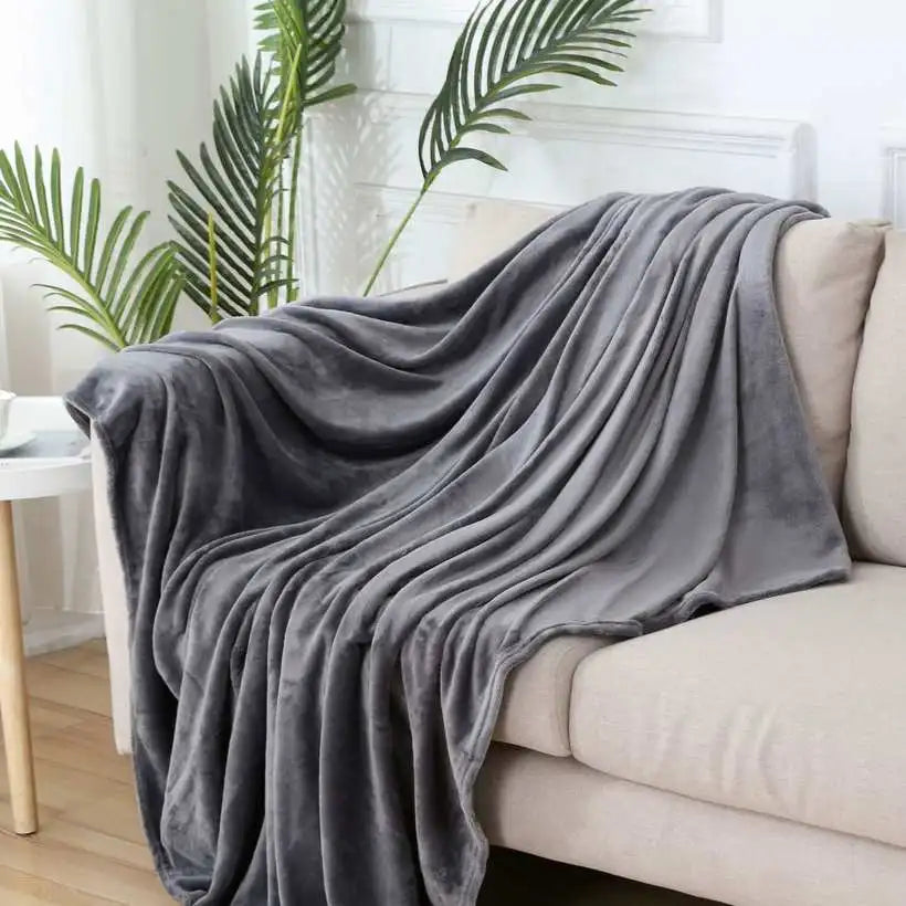 Gray blanket draped over a beige sofa in a living room with plants in the background