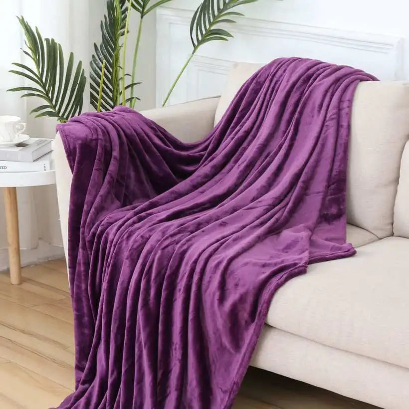Purple blanket draped over a white sofa in a living room setting with plants and a side table.