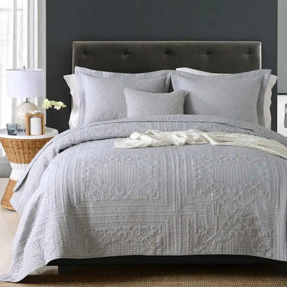 Gray quilted bedspread on a bed with a dark headboard in a bedroom setting.