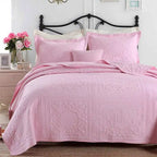 Pink bedspread set on a bed with a floral arrangement in the background