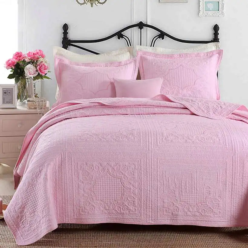 Pink bedspread set on a bed with a floral arrangement in the background