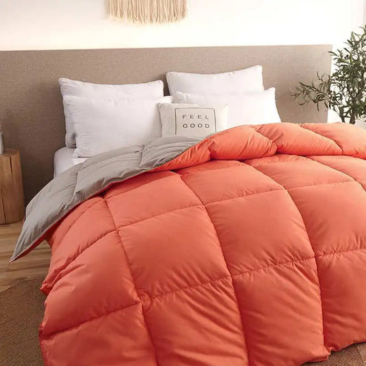Orange quilted comforter on a bed with white pillows and a plant in the background.