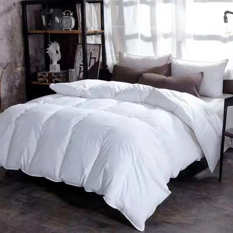 White comforter on a bed with pillows in a room with a bookshelf and window.